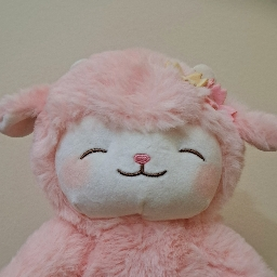A picture of a plushie of a sheep with pink wool on a white wall